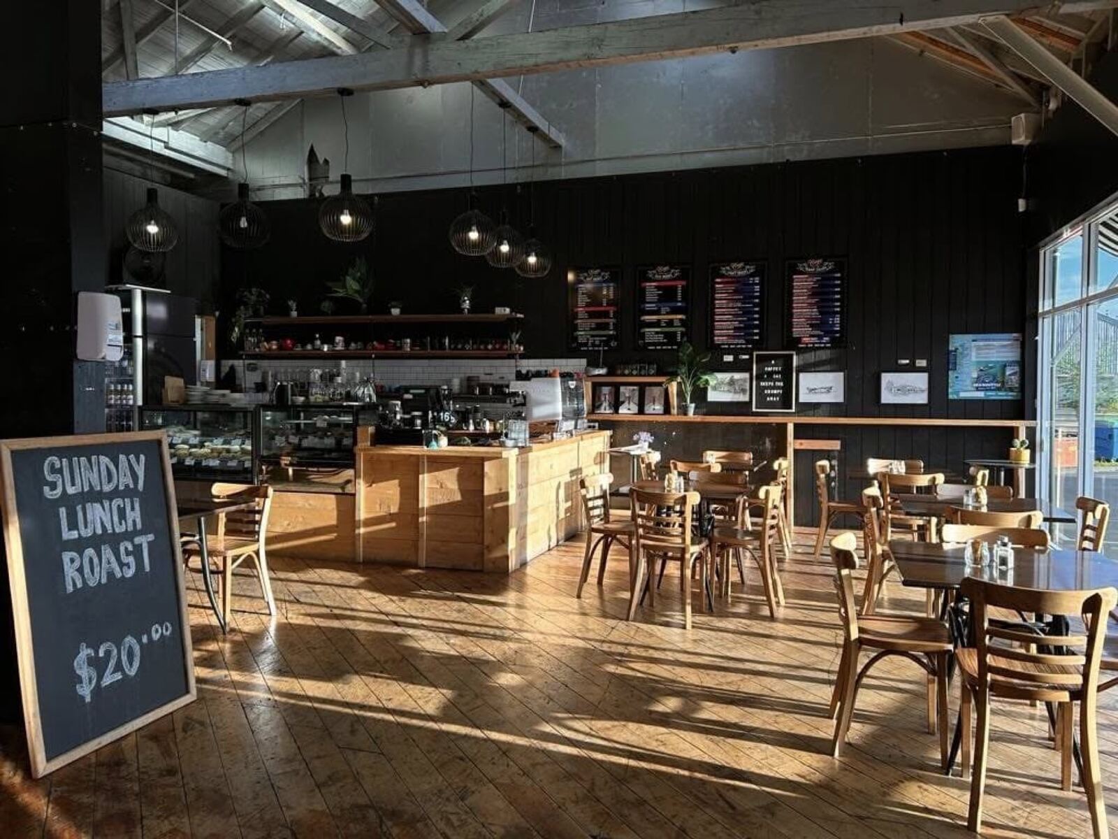 The Coops Cafe dining room: high white trussed rafters, black walls, timber floors and counter, pendant lights and a Sunday roast board